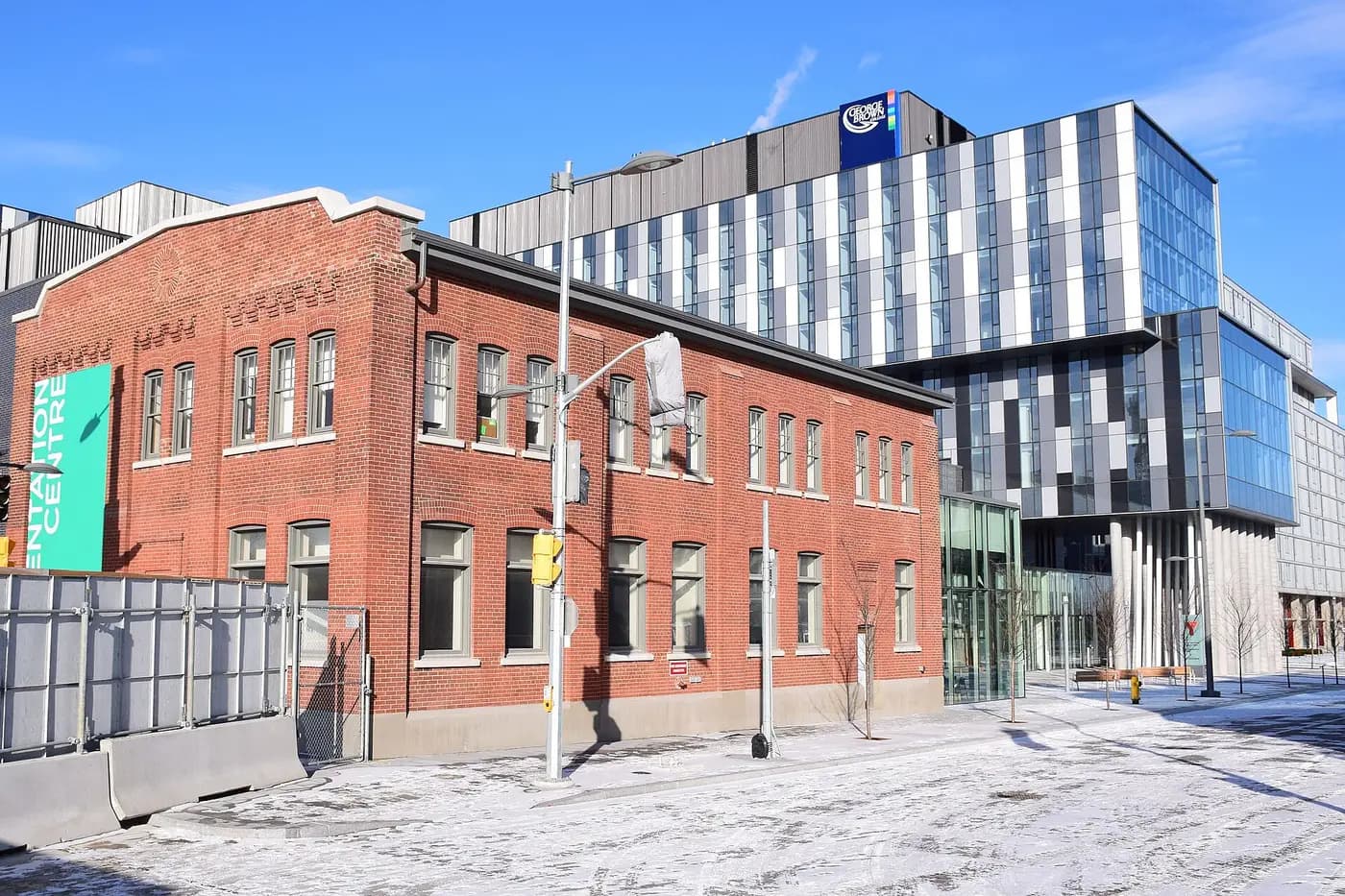 Glass residence tower with a George Brown sign behind the red-brick former CN Railway Police building
