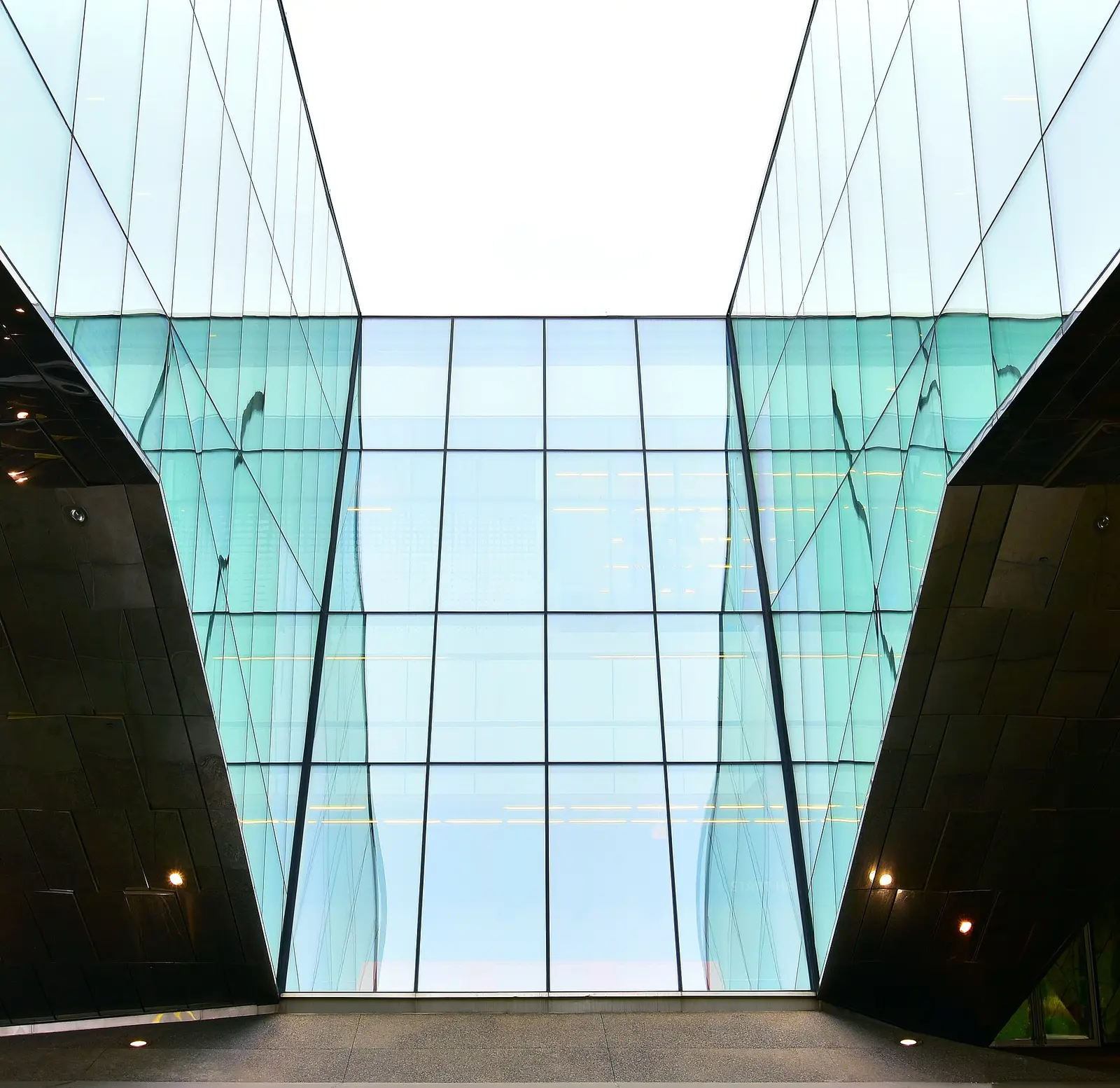 Two glass walls angling up toward the sky above a covered walkway at Centennial's Ashtonbee Campus