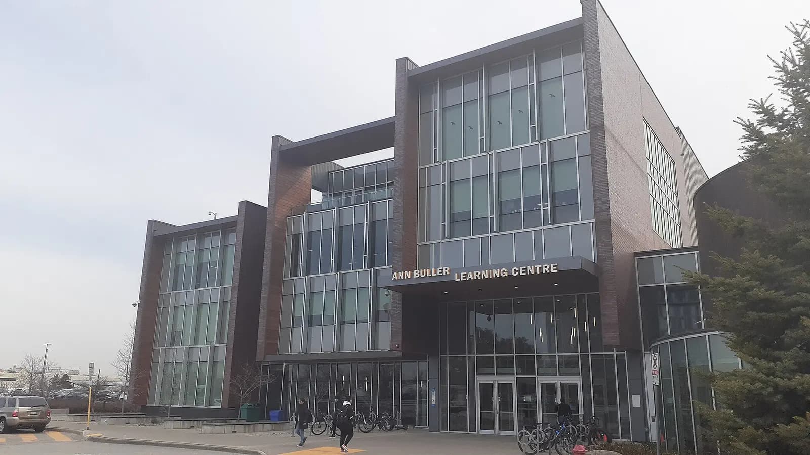 Brick and glass front of the Ann Buller Learning Centre at Centennial's Progress Campus, with students walking past bike racks