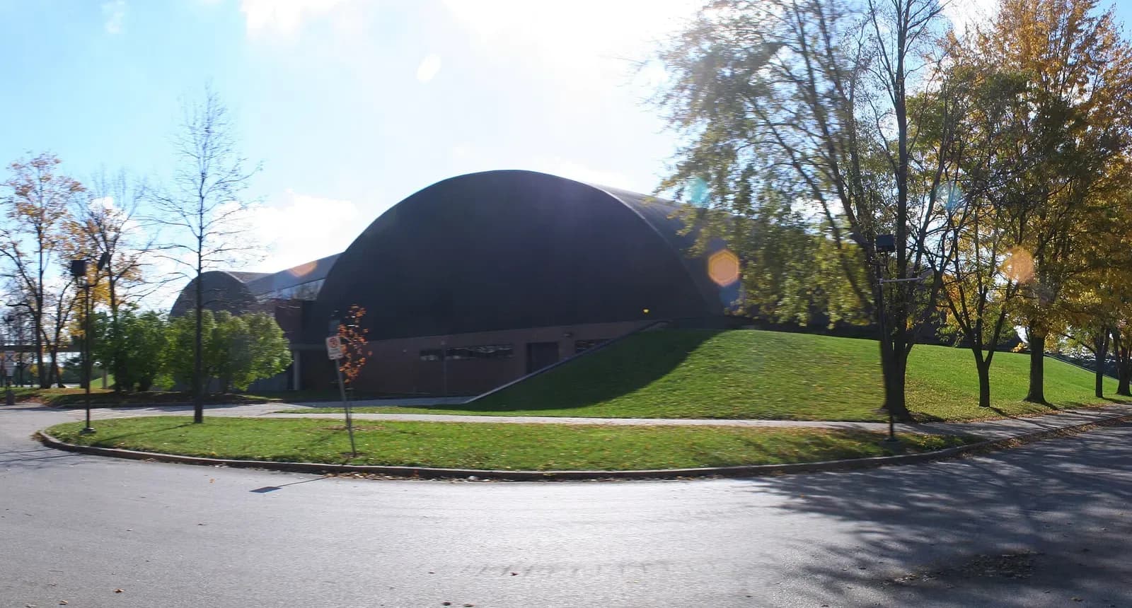 Domed recreation building behind a grassy slope and autumn trees at Conestoga's Doon Campus