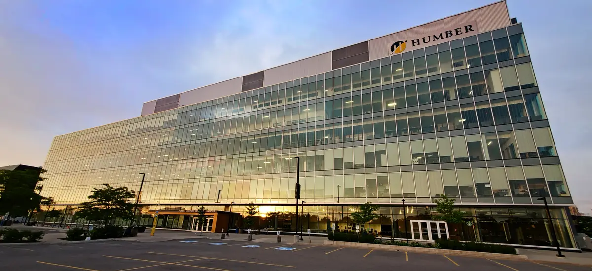 Glass facade of the Learning Resource Commons at Humber North Campus at sunset, with the Humber sign near the roof