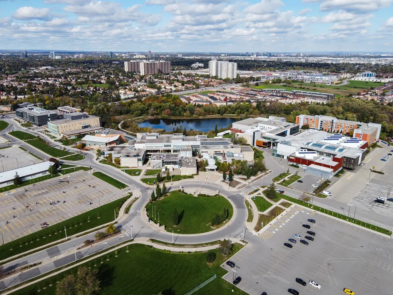 Aerial view of Sheridan's Davis Campus in Brampton, with a roundabout, parking lots and a pond behind the buildings