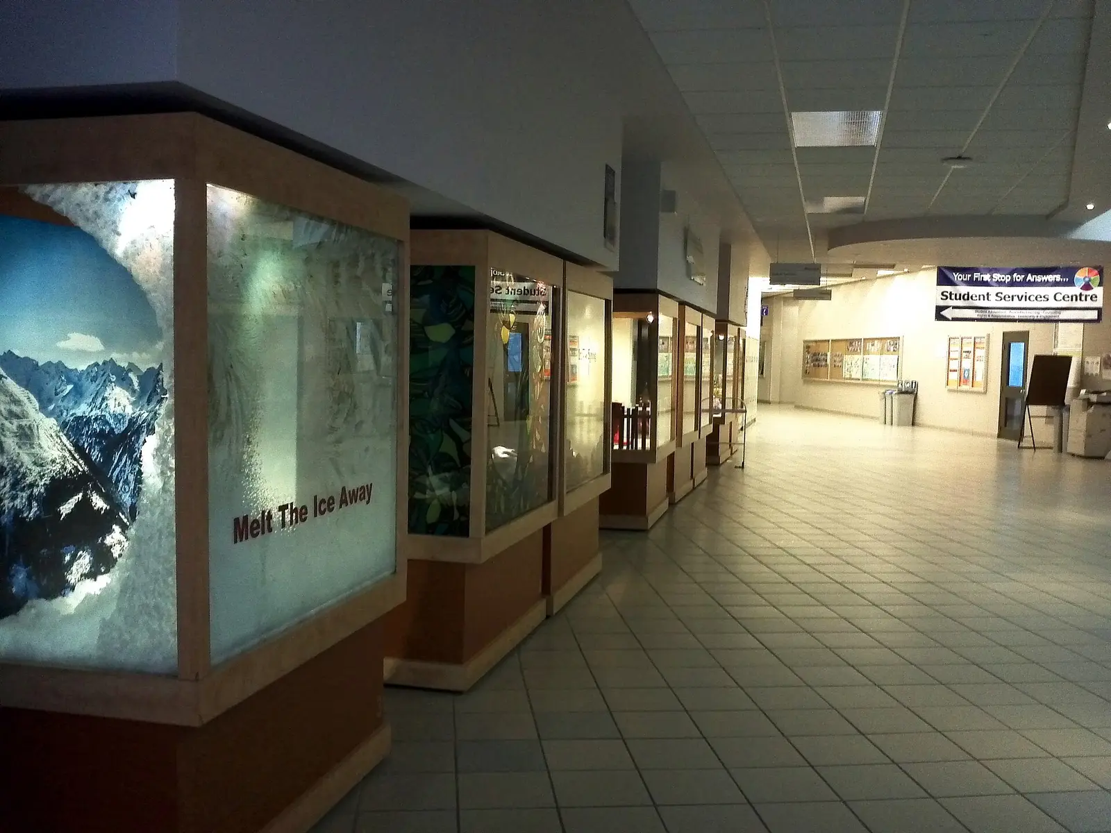 Tiled hallway at Sheridan's Trafalgar Campus with display cases and a sign pointing to the Student Services Centre