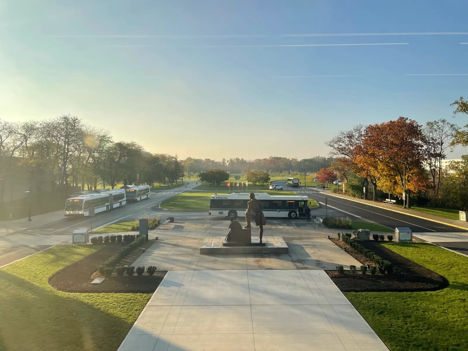 Morning view over the Sir Isaac Brock statue toward the campus bus loop, with St. Catharines Transit buses and autumn trees