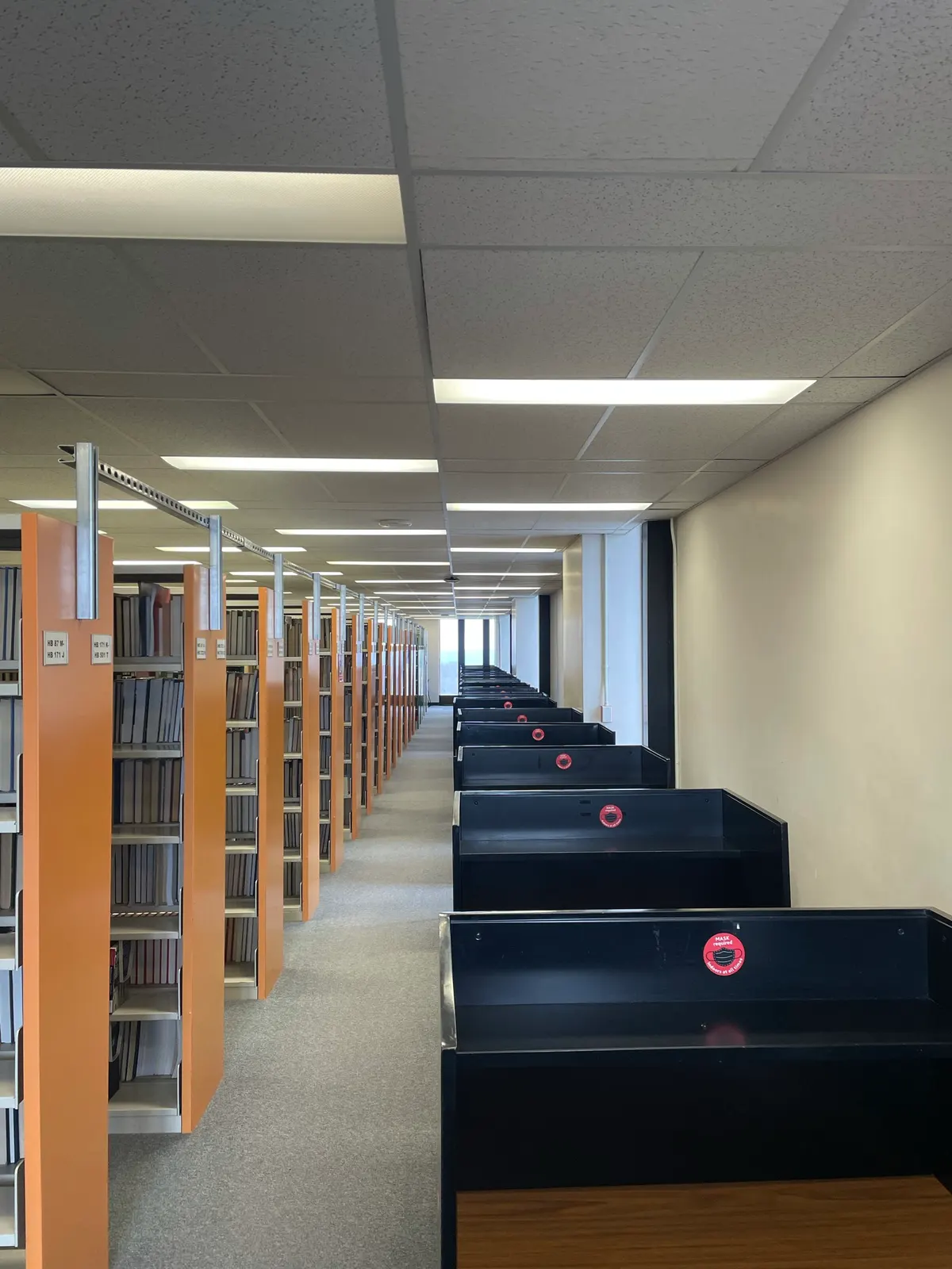 A long aisle of library shelving beside a row of study carrels on an upper floor of Schmon Tower