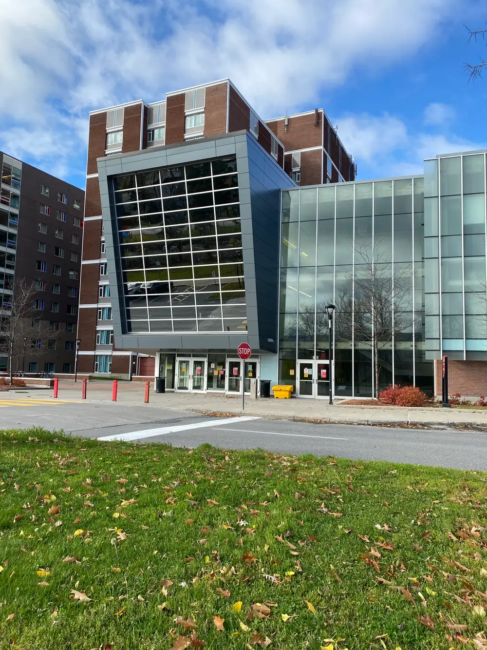 Glass-fronted Residence Commons building with an angled dark window box, in front of red-brick residence towers in autumn