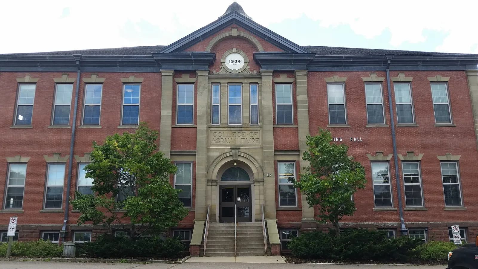 Red-brick Cumming Hall on Dalhousie's Agricultural Campus, with sandstone trim, an arched central doorway, front steps and two small trees