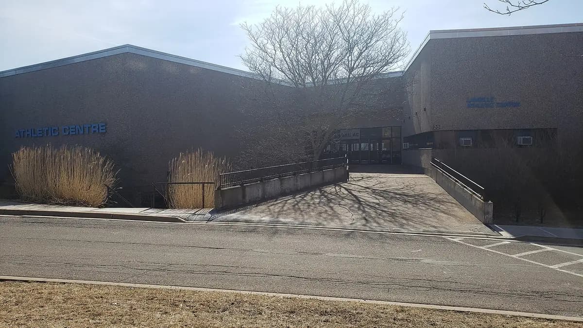 Low brown brick Langille Athletic Centre on Dalhousie's Truro campus, with blue Athletic Centre lettering, an entrance ramp and a bare tree
