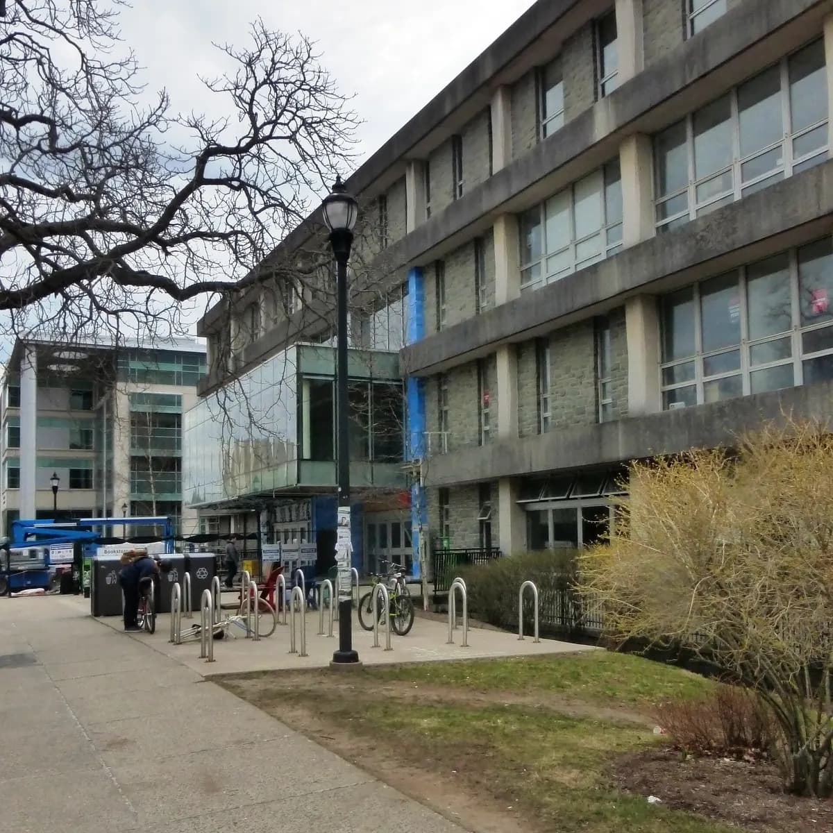 Dalhousie's Student Union Building, a stone and concrete building with a glass entrance, bike racks and a lamp post in front and a bare tree overhead