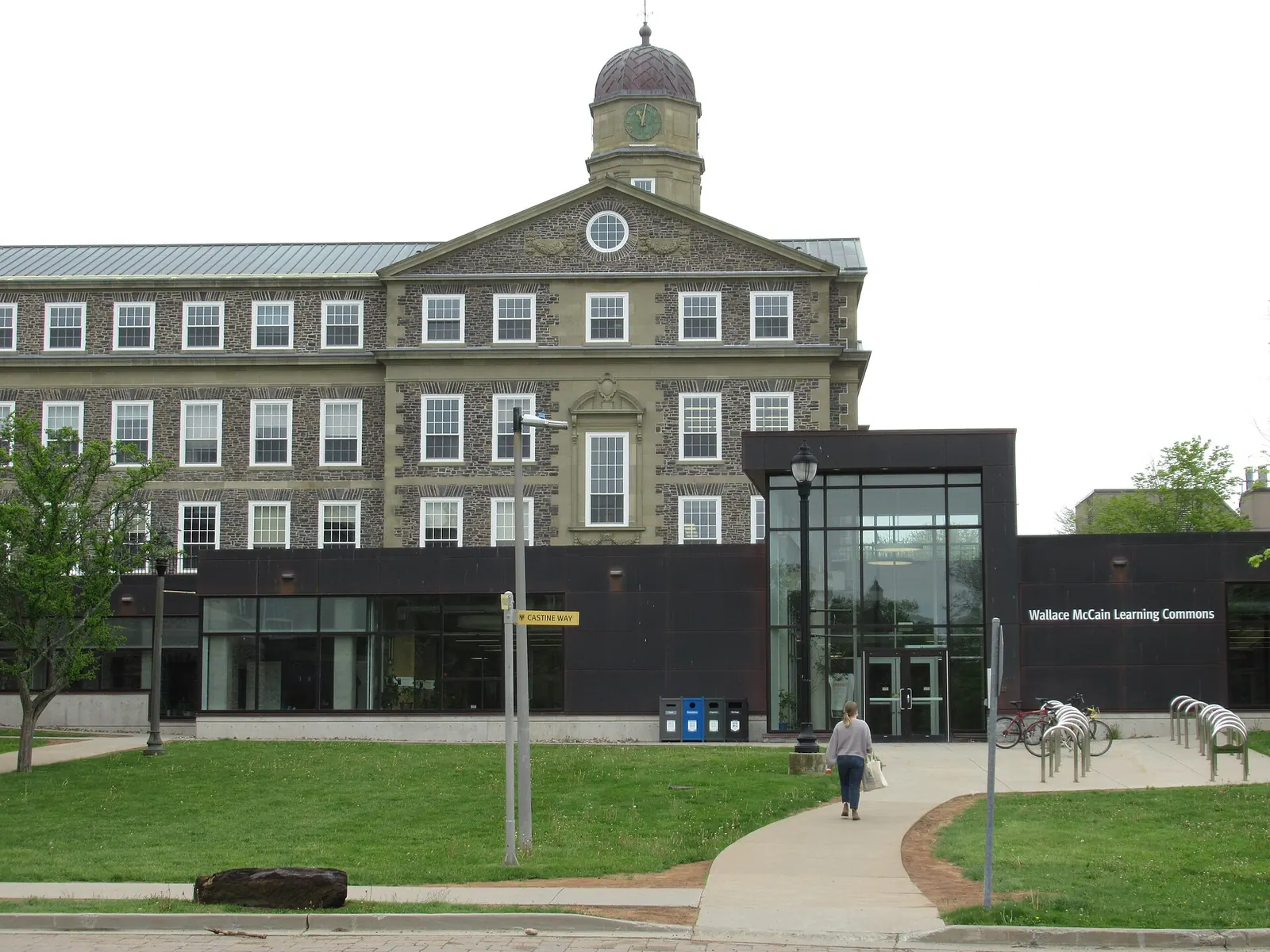 Dark glass-fronted Wallace McCain Learning Commons at Dalhousie, with a lawn and walkway in front and the stone Henry Hicks Building and its clock tower behind