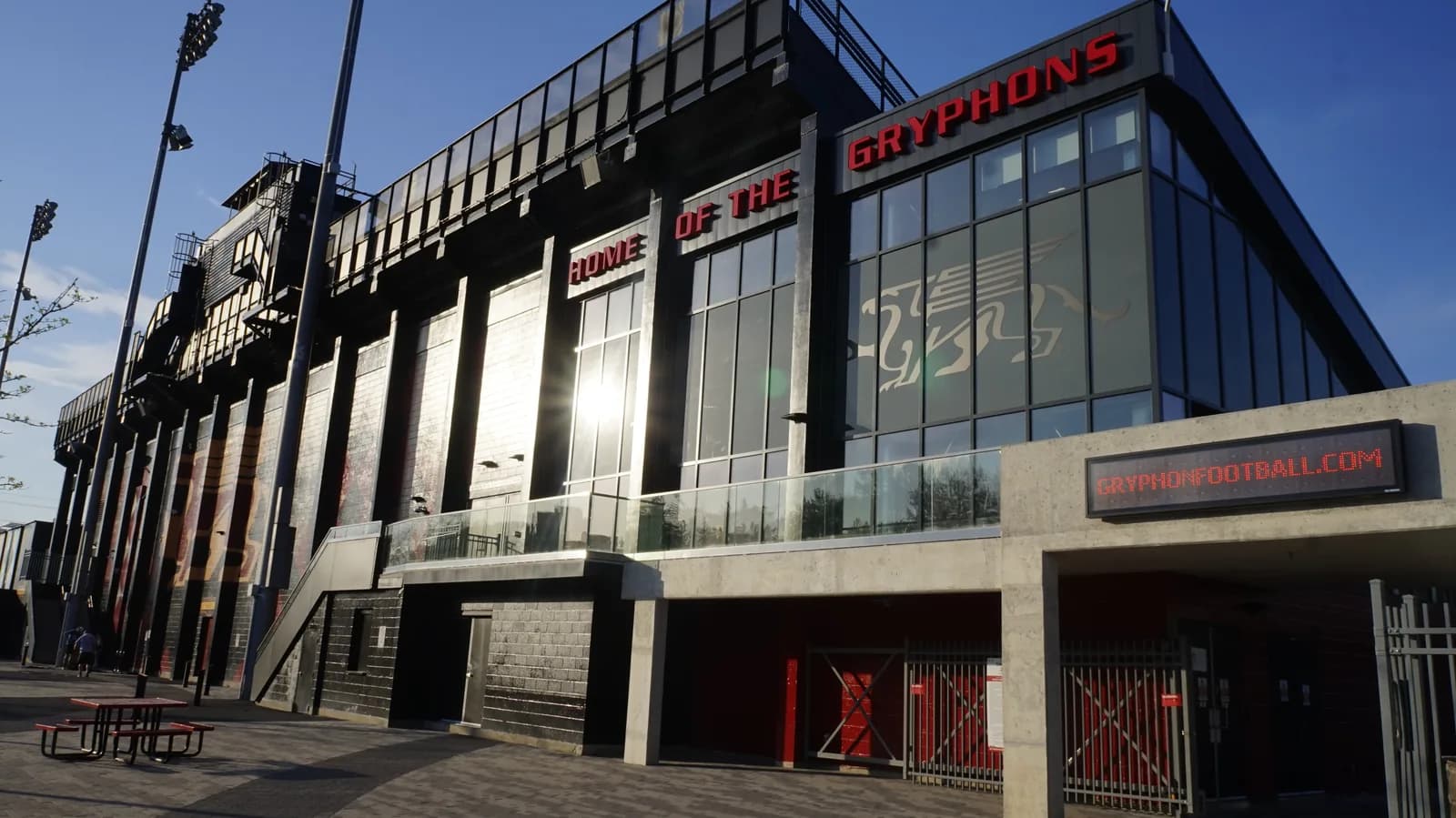 Outside wall of Guelph's Alumni Stadium with red lettering reading Home of the Gryphons, a gryphon graphic on the glass and floodlight masts