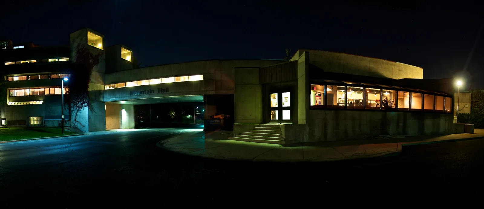 Night view of Mountain Hall in Guelph's South Residence, a concrete building with its name on a bridge over a driveway and lit window bands