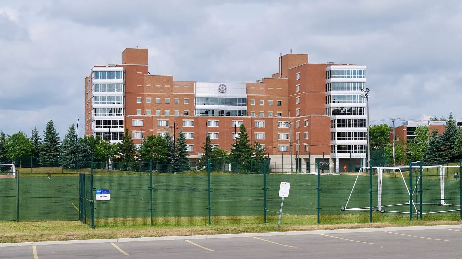 Red-brick King Street Residence at Laurier's Waterloo campus, with glass stair towers, seen across a fenced turf field