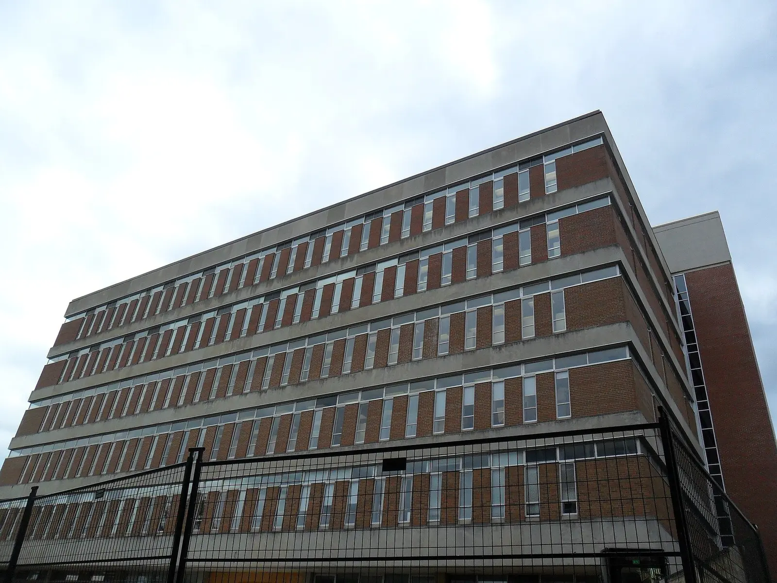 Brick and concrete upper floors of Laurier's Waterloo campus library behind a construction fence