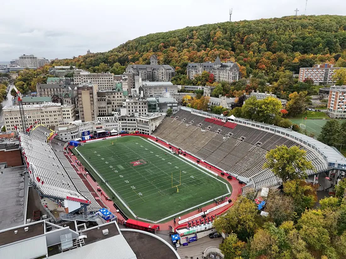 Aerial view of Percival Molson Memorial Stadium's turf field and red track, with McGill's downtown campus and Mount Royal behind