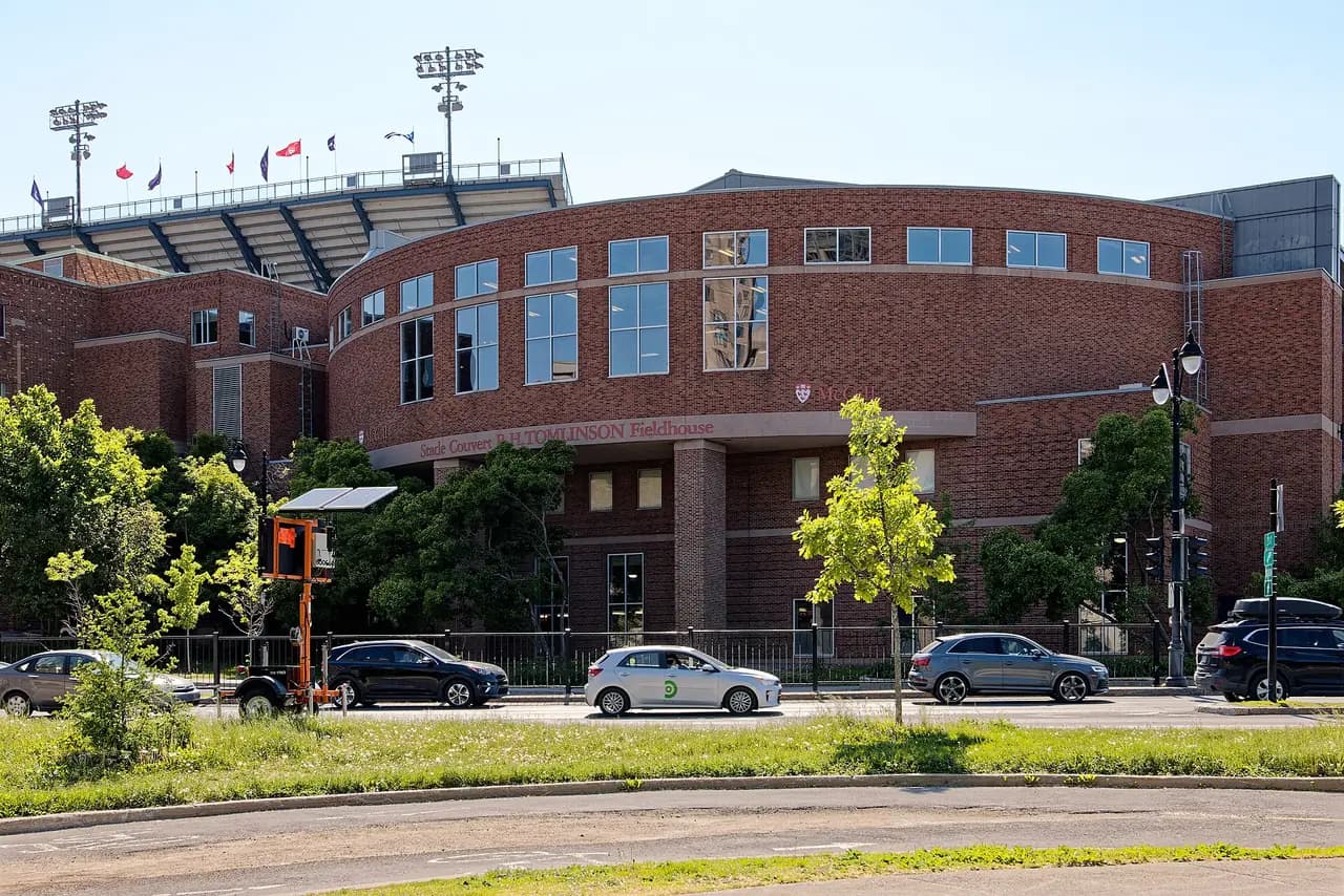 Red-brick curved facade of McGill's Tomlinson Fieldhouse on Pine Avenue, with Molson Stadium stands and floodlights behind