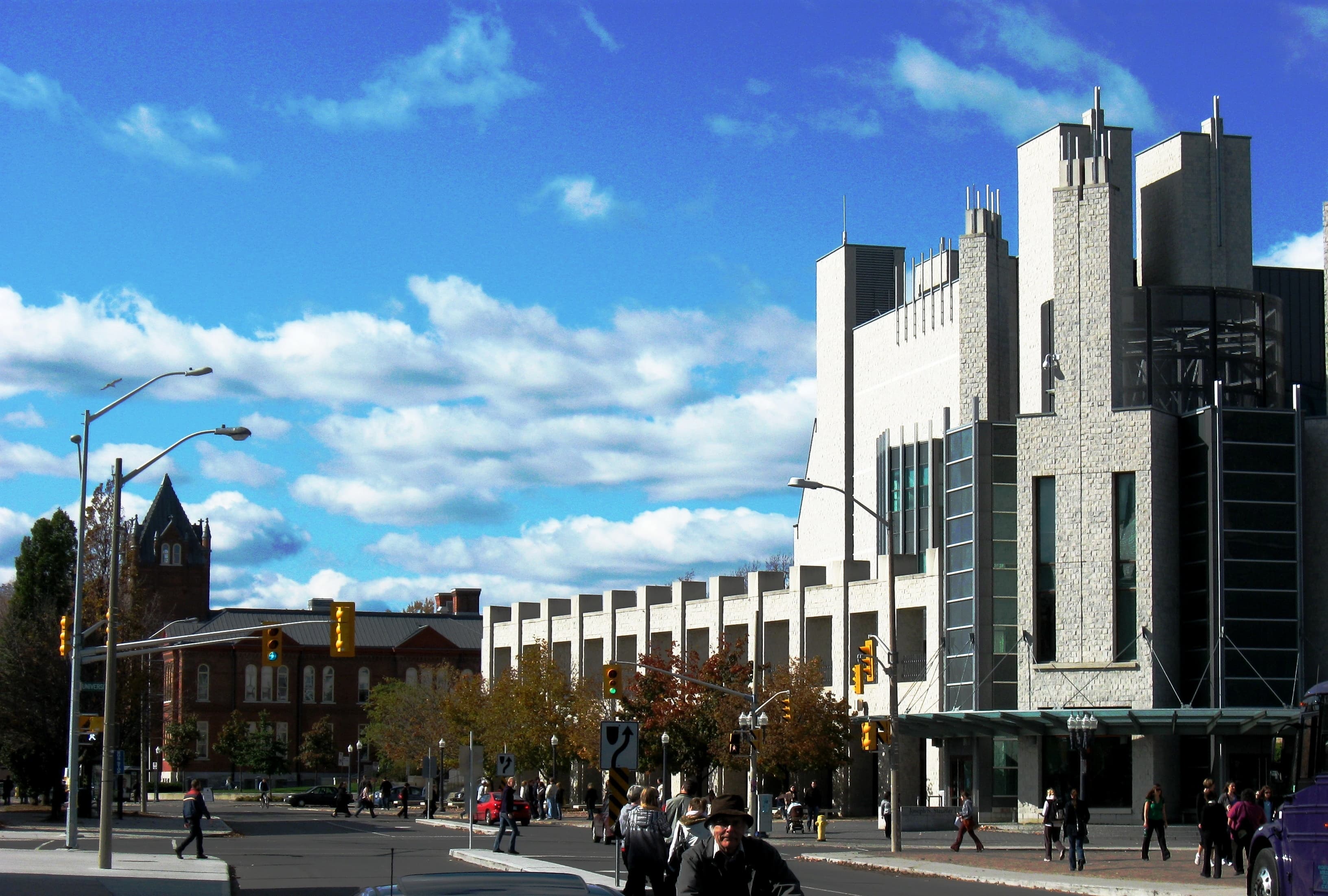 Pale stone walls and tall windows of Queen’s Stauffer Library beside a street intersection