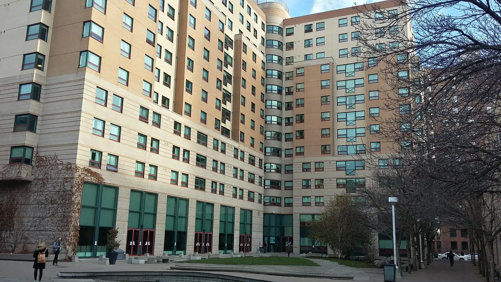 Tall tan-brick Pitman Hall residence with a rounded corner tower, green ground-floor windows and a paved courtyard with a small lawn