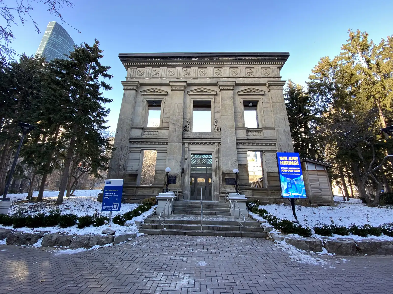 Historic stone facade with steps and glass doors leading down to TMU's underground Recreation and Athletics Centre, with a blue RAC 40/50 Gould St sign