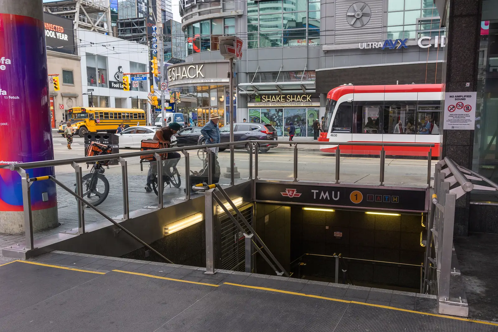 Stairway entrance to the subway with an overhead TTC sign reading TMU and Line 1, and a red-and-white streetcar on the street behind