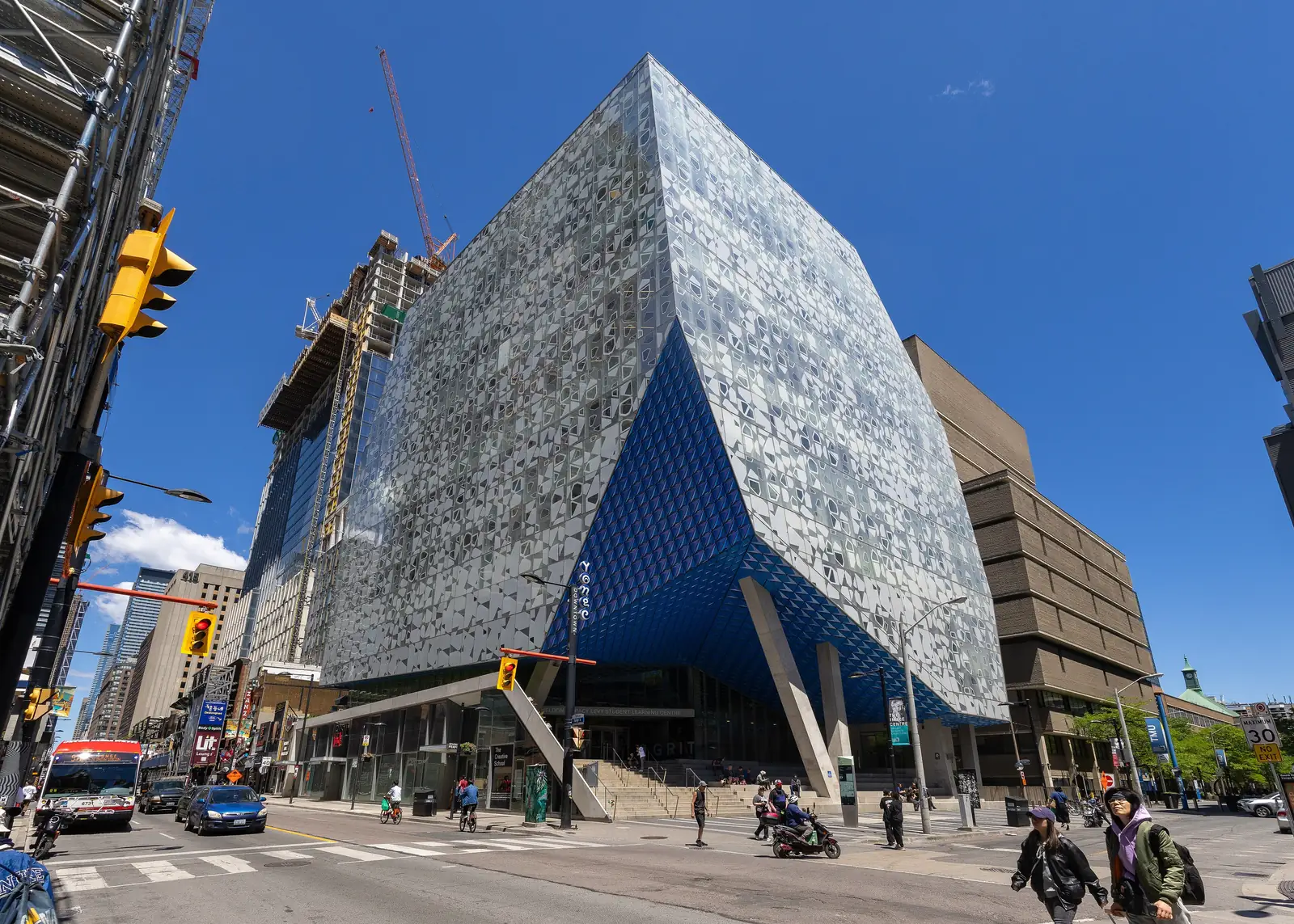 Patterned glass Student Learning Centre at Yonge and Gould streets with a blue faceted underside over the entrance steps, and the concrete Library Building behind it