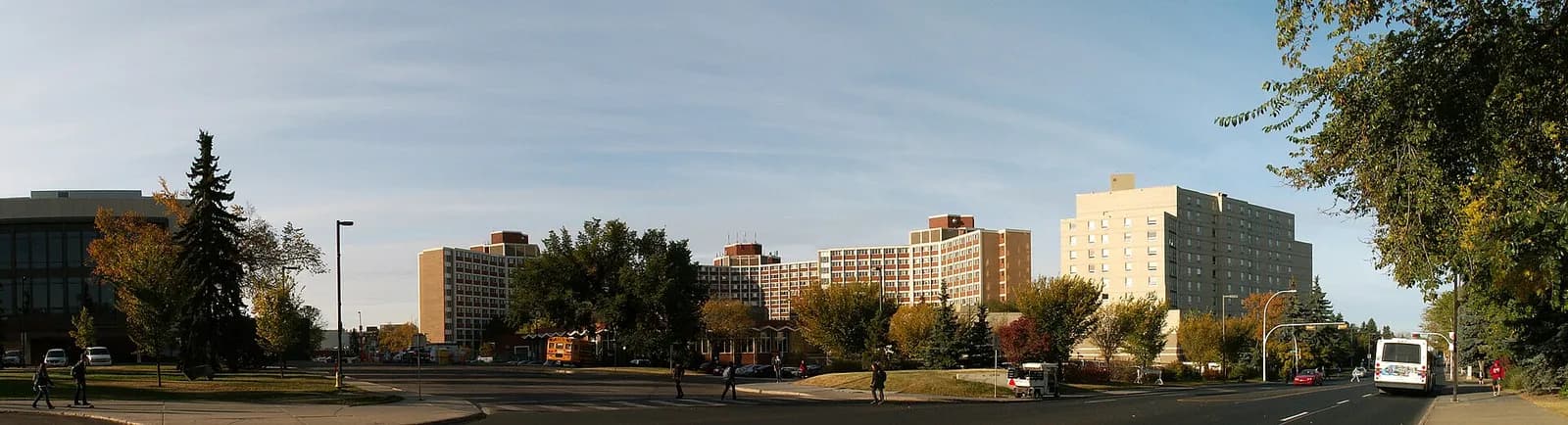 Panorama of the brick Lister residence towers behind autumn trees on 87 Avenue, with a transit bus on the right and the Jubilee Auditorium at the left edge
