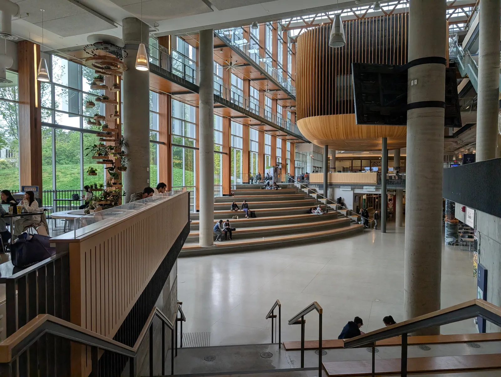 Multi-storey atrium of the AMS Student Nest with wide wooden stair seating, wood panelling and students studying