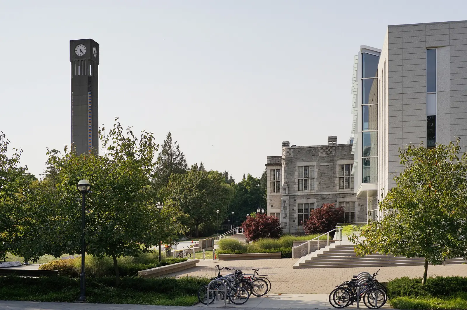 UBC clock tower beside the stone core and glass wing of the Irving K. Barber Learning Centre, with bikes parked on the plaza
