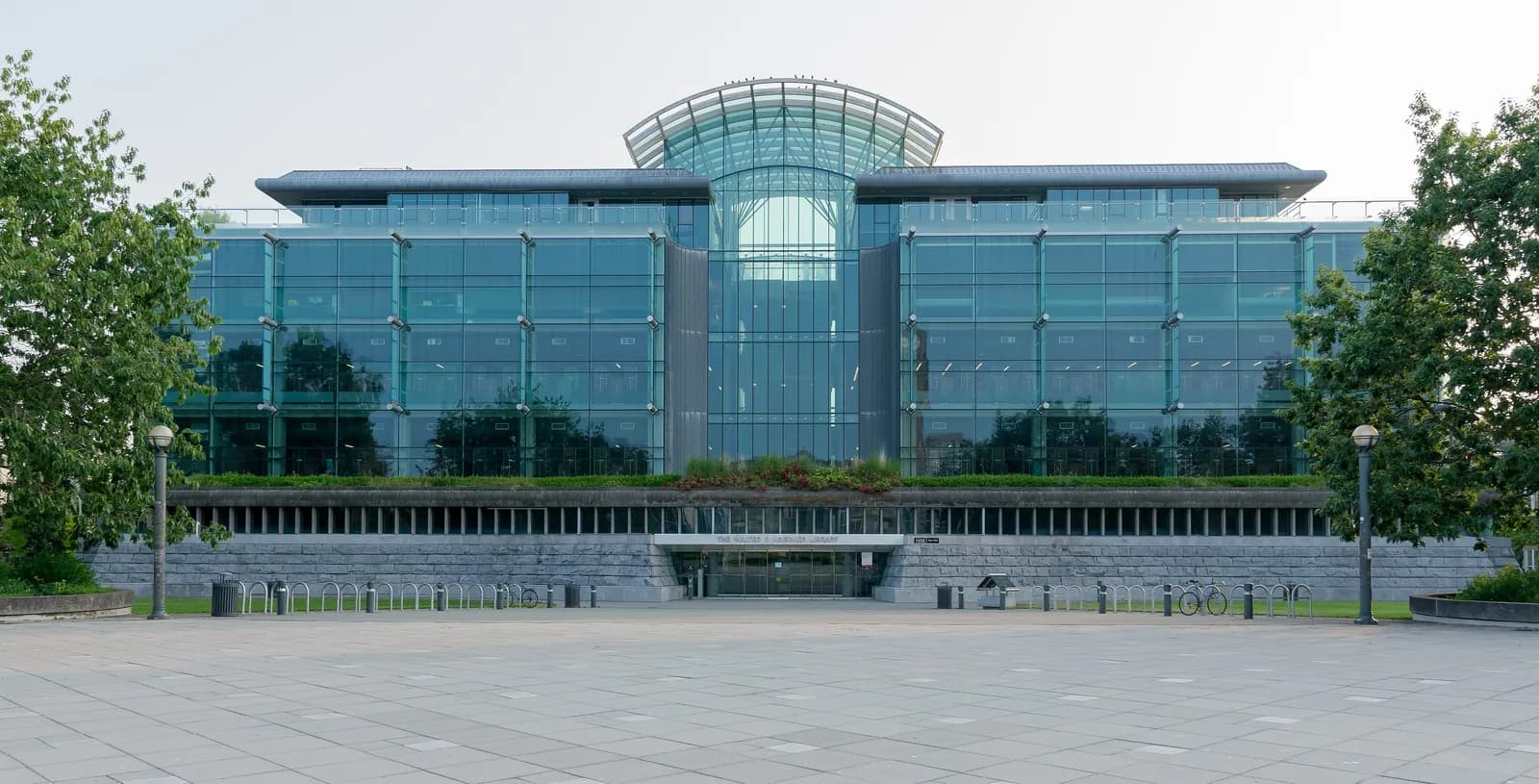 Glass facade and curved roof of Walter C. Koerner Library at UBC Vancouver, seen across a paved plaza