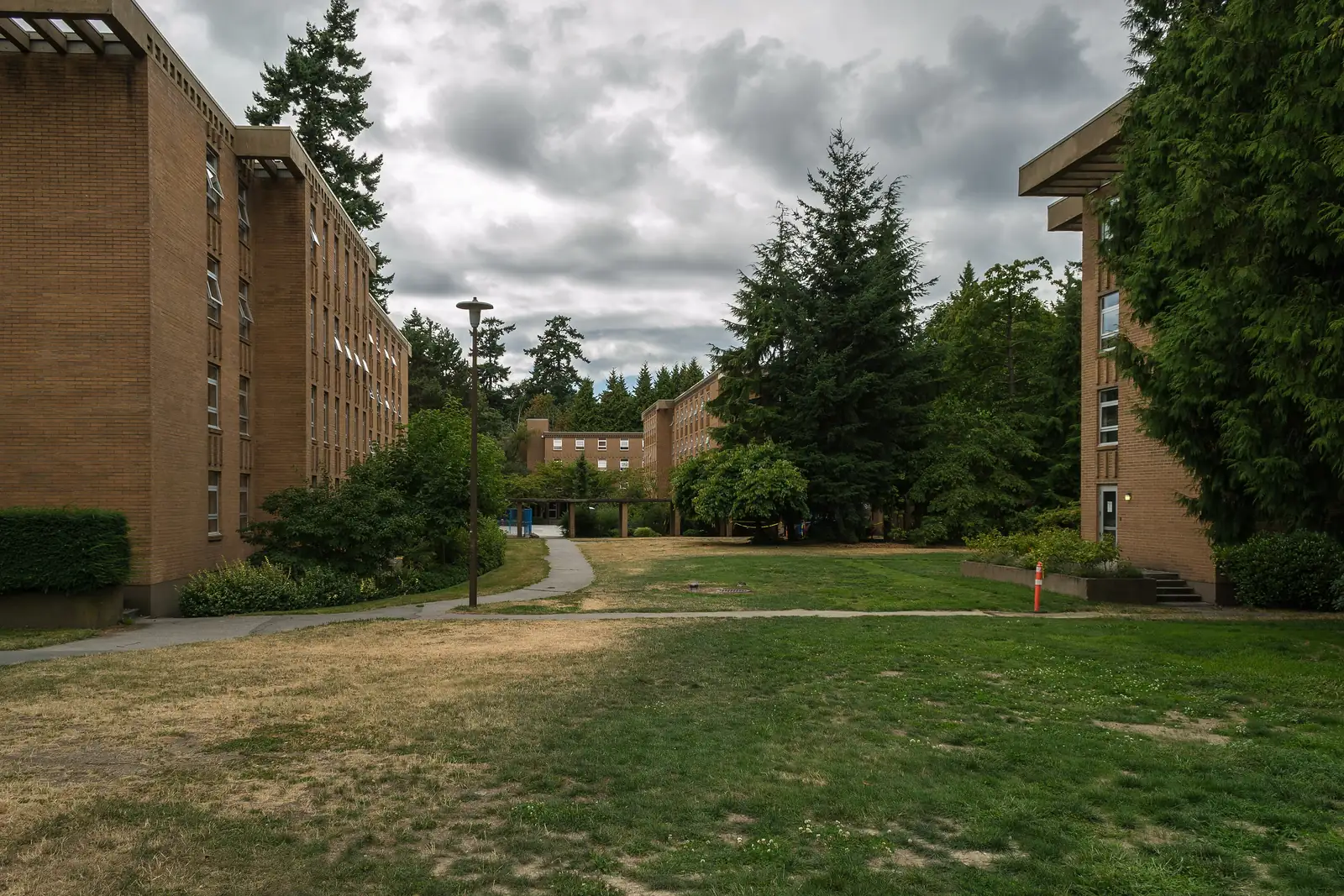 Brick Place Vanier residence buildings around a lawn with tall evergreen trees at UBC Vancouver