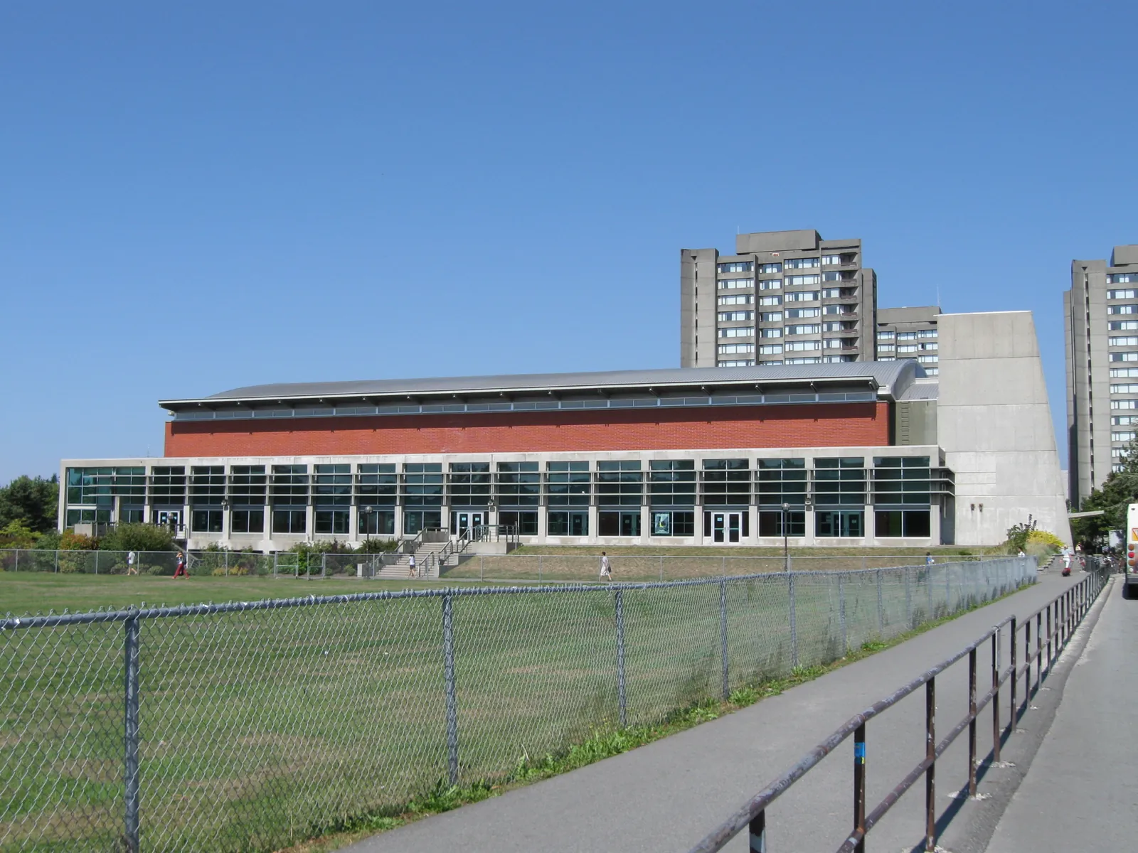 Low red-brick and glass Student Recreation Centre at UBC Vancouver beside a playing field, with residence towers behind