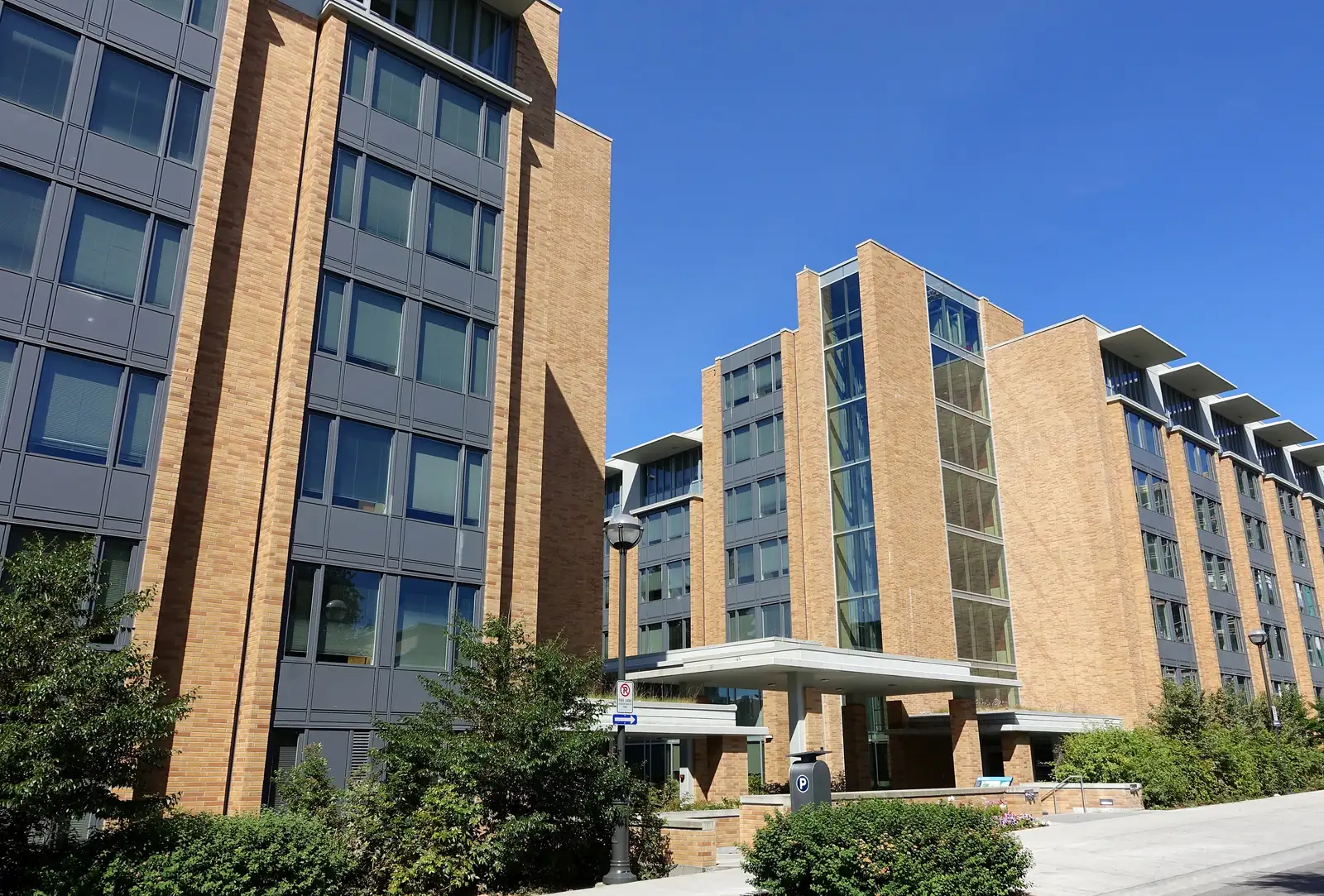Tan-brick and grey-panel residence houses at Totem Park, UBC Vancouver, with a covered entrance under a blue sky