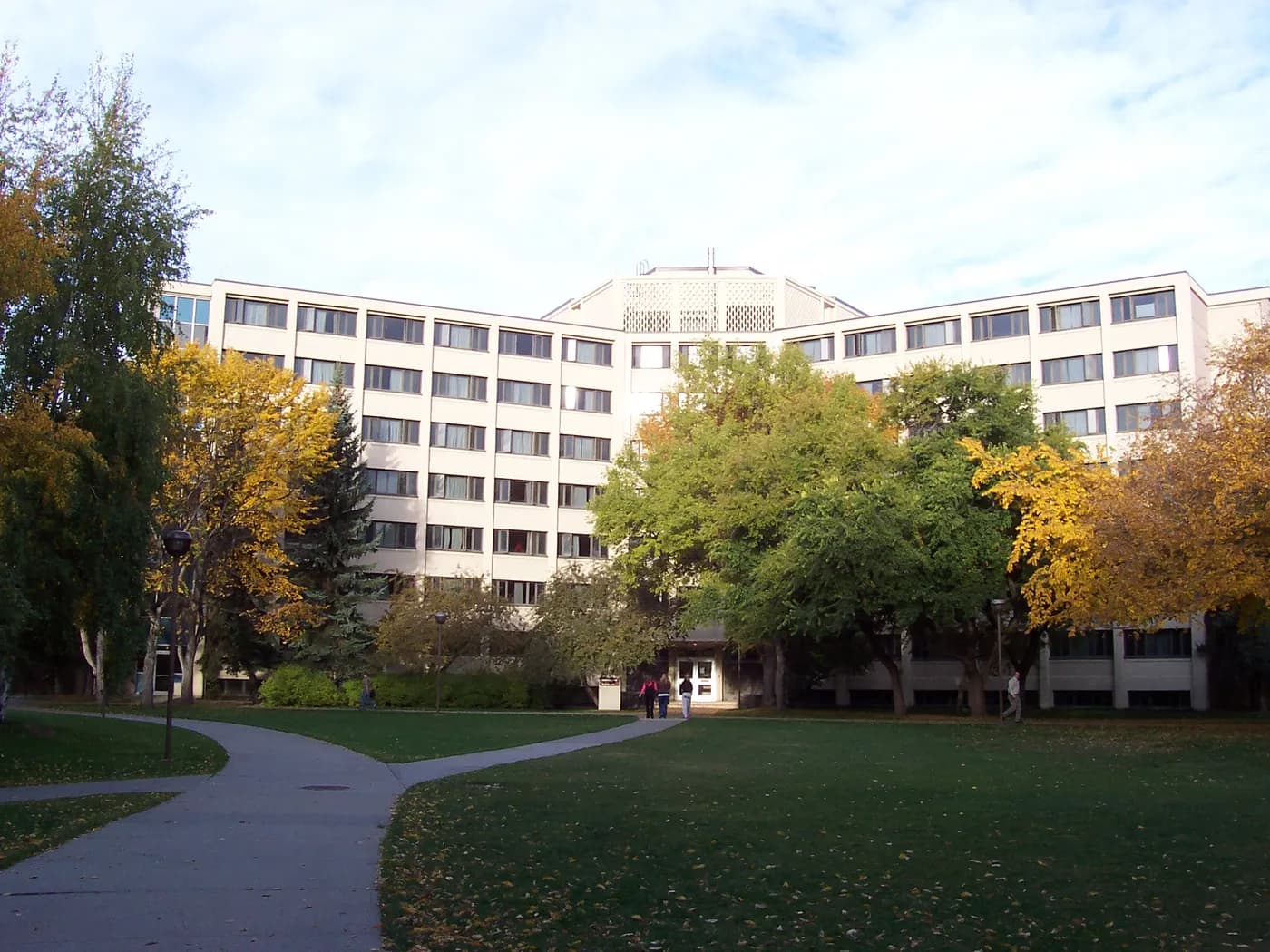Long pale residence block of Kananaskis Hall at UCalgary behind autumn trees, a lawn and a curving path