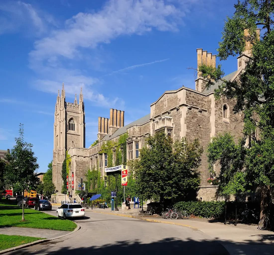 Hart House's grey stone Gothic building with tall chimneys and a stone tower at the far end, beside a curving campus road