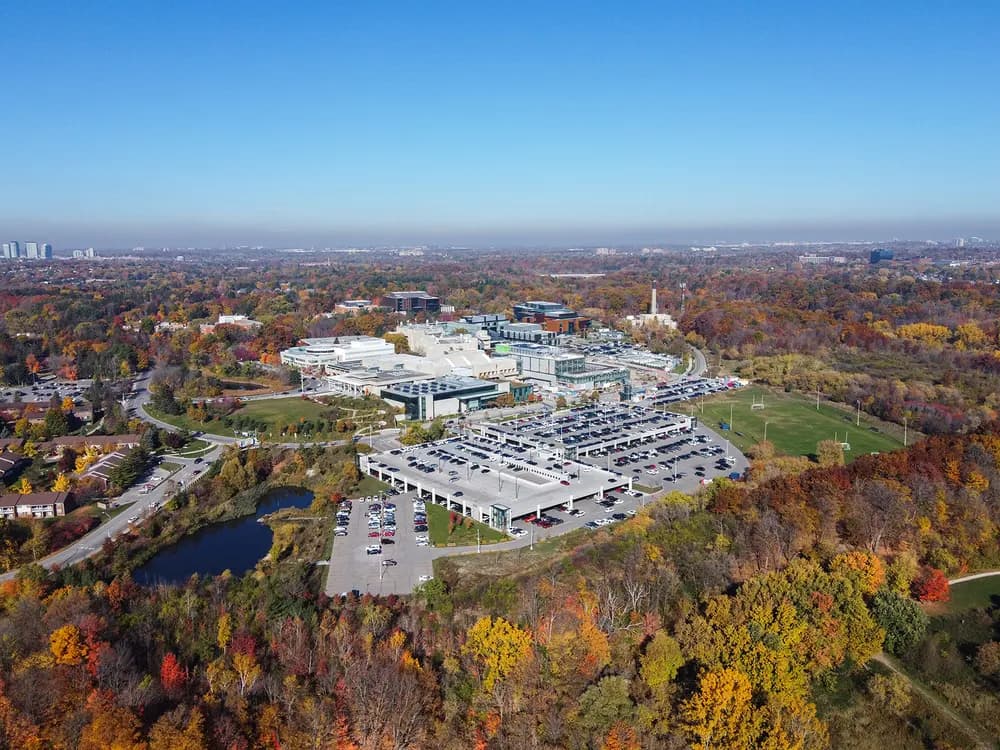 Aerial view of U of T Mississauga's buildings, playing field and surrounding autumn woodland
