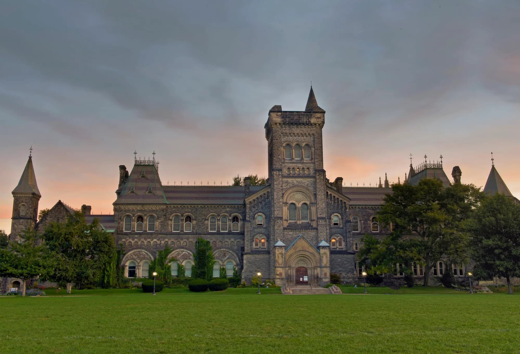 Romanesque stone facade and central tower of University College across a green lawn at U of T St. George