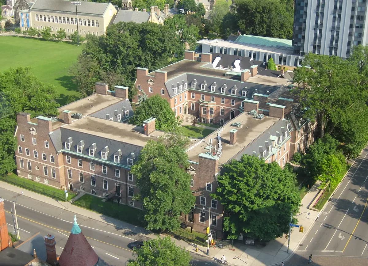 Aerial view of Whitney Hall's red-brick residence wings with dormer windows around a green courtyard, with a street and trees in front