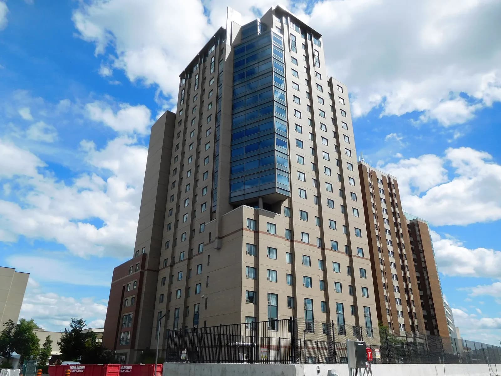 The 20-storey tan-brick 90 University residence tower at uOttawa with a blue glass central column, seen from below