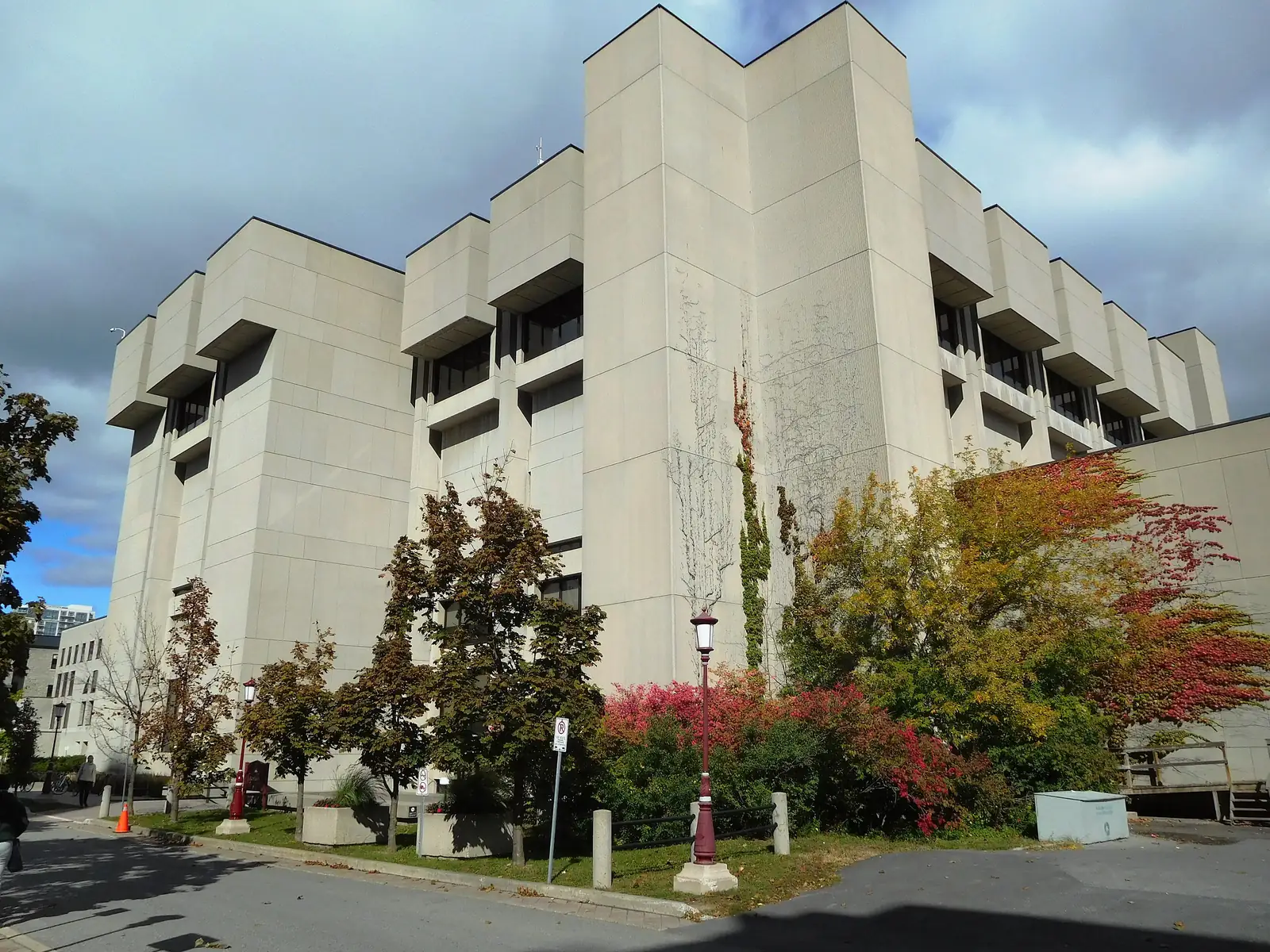 Pale concrete Brutalist exterior of Morisset Hall, home of uOttawa's Morisset Library, with autumn trees and a red campus lamppost