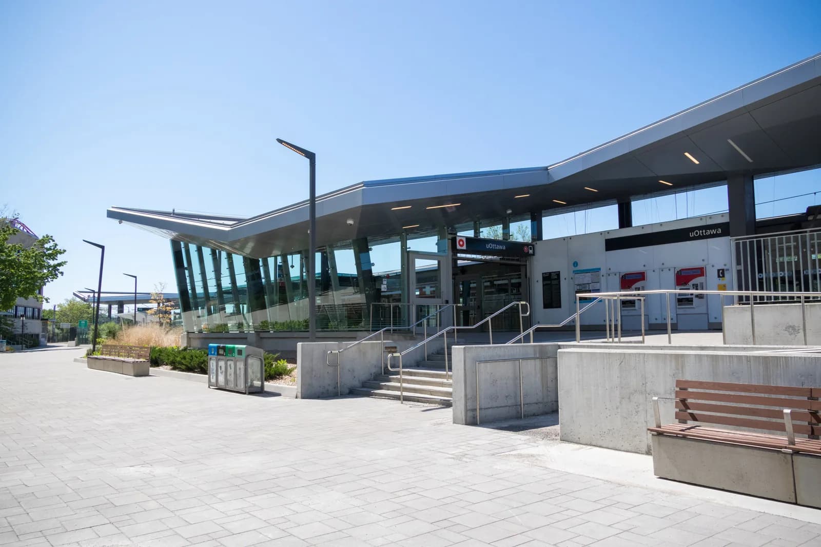 Entrance to uOttawa O-Train station with an angled canopy, glass walls, uOttawa signs, steps and an empty paved plaza