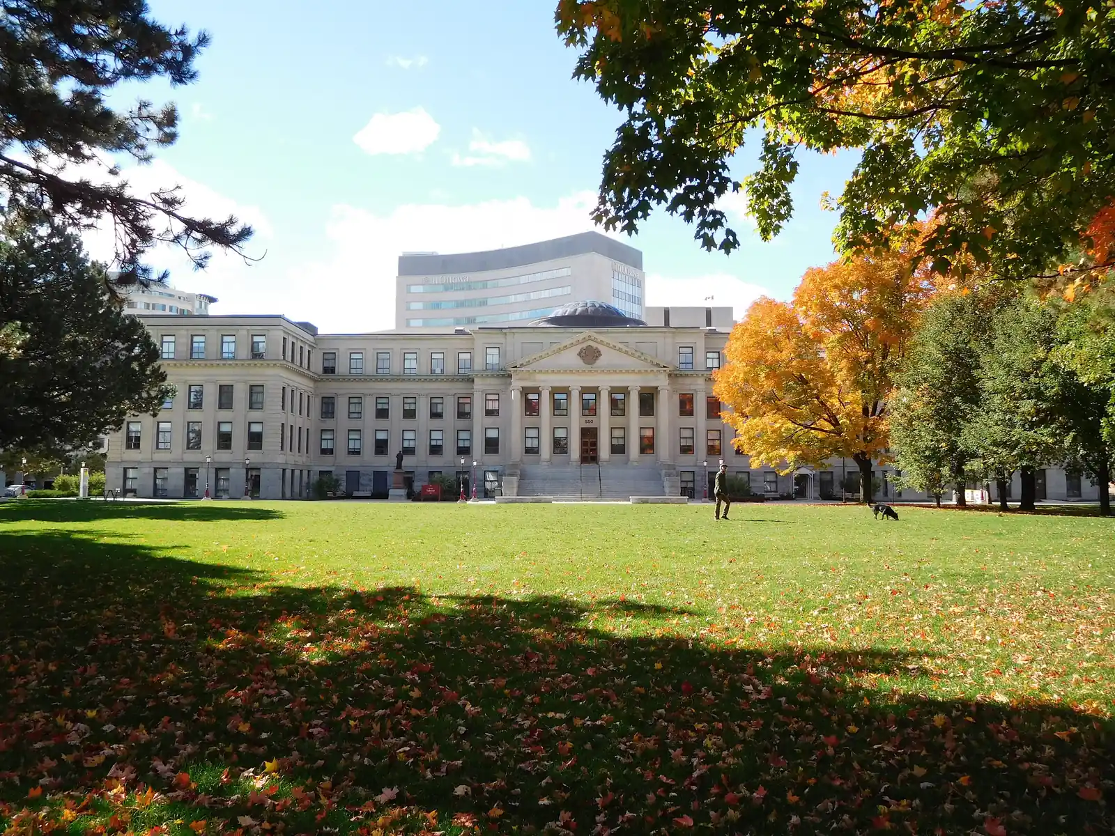 Neoclassical columned front of Tabaret Hall at uOttawa across a green lawn with autumn maples, the Desmarais tower behind