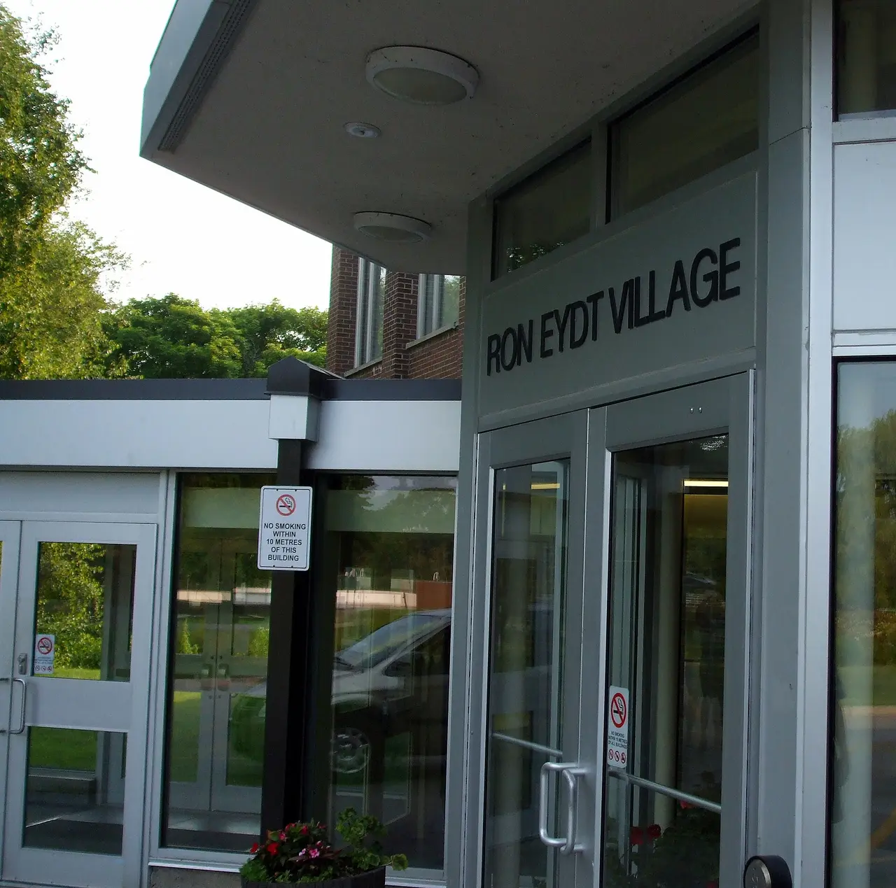 Glass entrance doors under a canopy with the sign Ron Eydt Village at the University of Waterloo