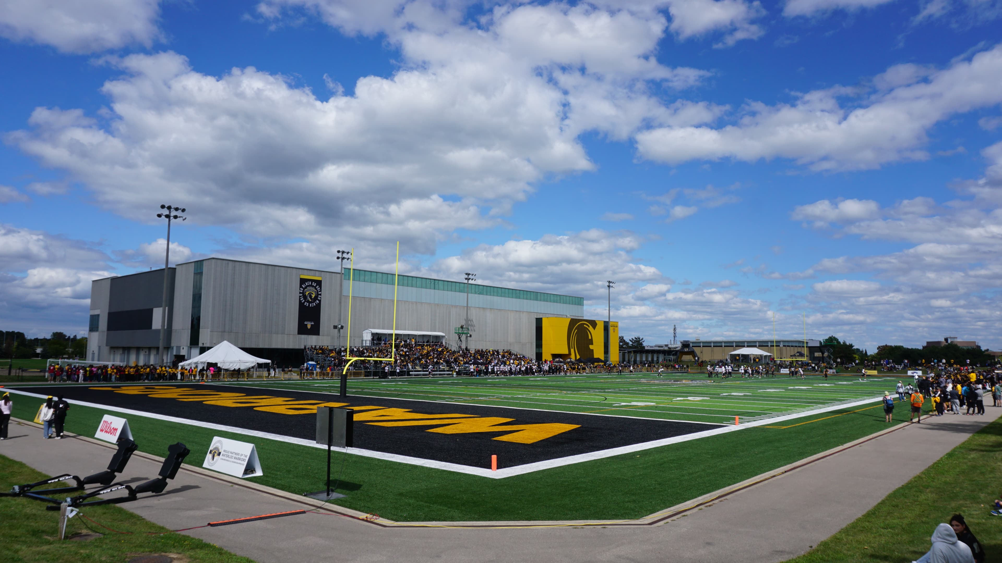 Waterloo Warriors football game on the turf at Warrior Field with spectators and a building behind it