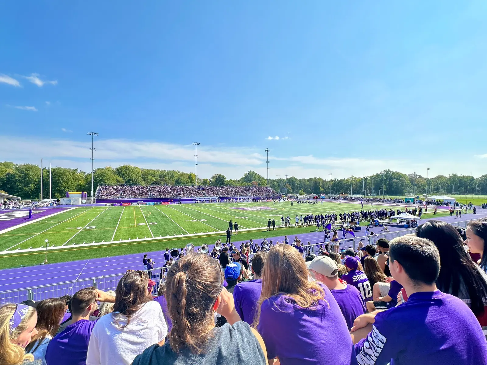 Fans in purple watching a Western Mustangs football game at Western Alumni Stadium, with the purple track and turf field