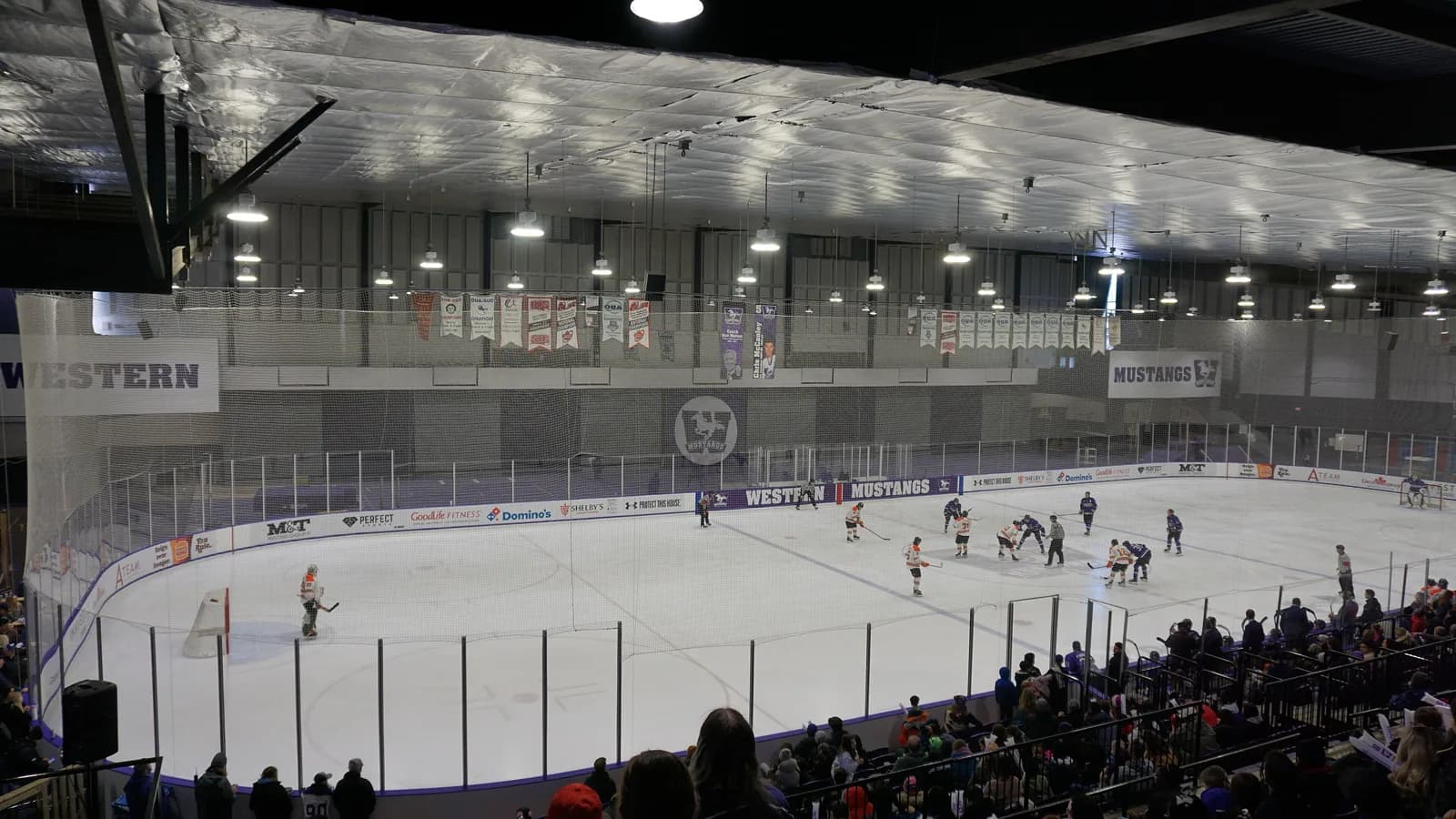 Faceoff during a Western Mustangs hockey game at Thompson Arena, with Western signage, banners and spectators