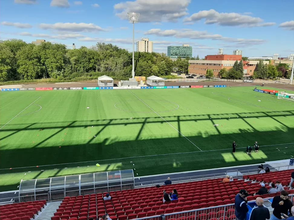 Turf field at York Lions Stadium seen from red stands, with campus buildings and trees behind