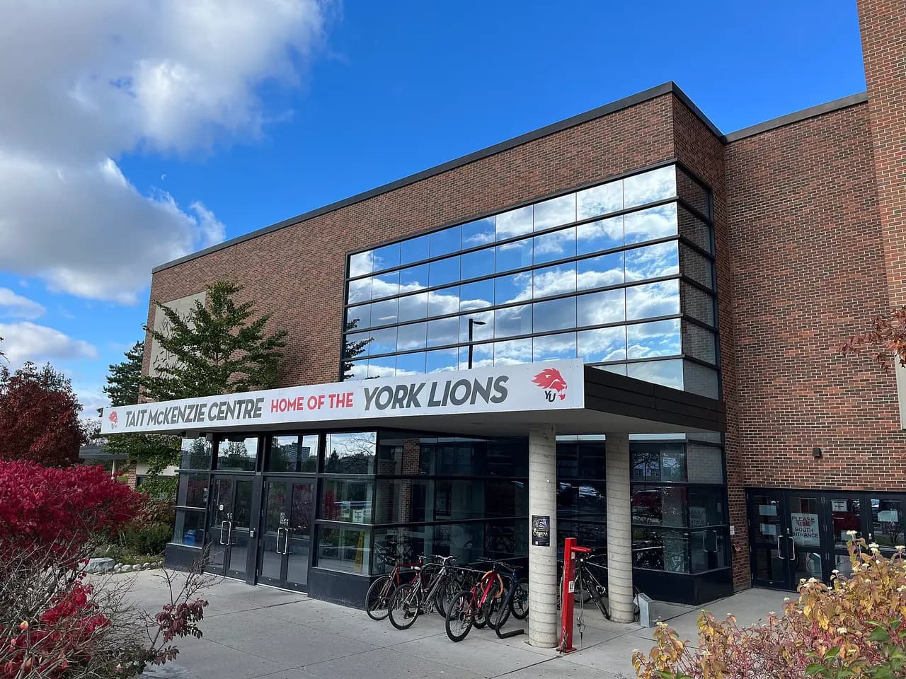 Brick and glass entrance of the Tait McKenzie Centre with a Home of the York Lions banner and bikes parked outside