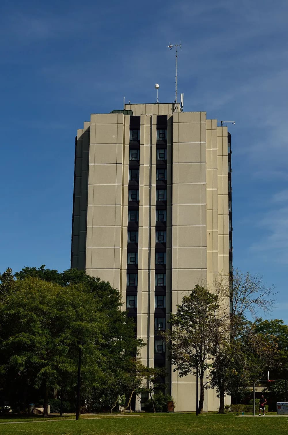 Vanier Residence, a 13-storey concrete tower on York's Keele campus, behind trees and a lawn